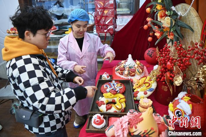 1月25日，隨著春節(jié)臨近，蘭州一花饃店“龍”元素花饃熱銷。圖為工作人員向顧客推薦“龍”元素花饃。九美旦增 攝</p><p>